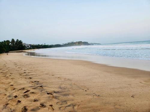 a beach with footprints in the sand and the ocean at Seven Shape Resort - Talalla in Talalla