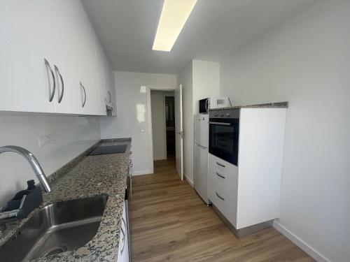 eine Küche mit weißen Schränken, einer Spüle und einem Kühlschrank in der Unterkunft Wind Rose Gandia Beach in Playa de Gandia