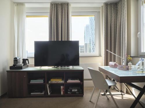 a living room with a tv and a table and a desk at Flemings Selection Hotel Frankfurt-City in Frankfurt/Main
