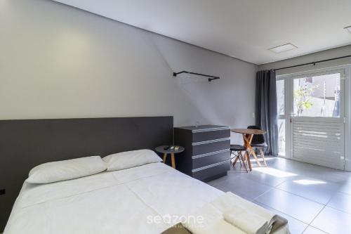 a bedroom with a bed and a desk and a window at Estúdio Modernos em Condomínio com Piscina em Floripa - ASK in Florianópolis