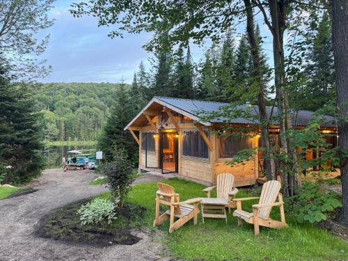 a cabin in the woods with chairs and a table at Huttopia Les Deux Lacs - Laurentides in Mont-Blanc