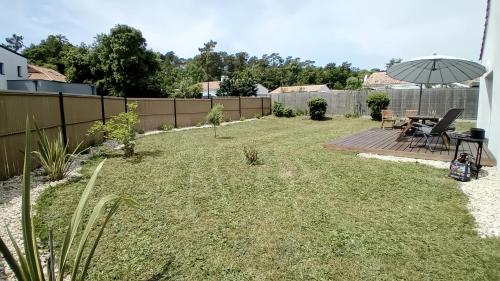 une cour avec une clôture, une table et un parasol dans l'établissement Au pied de la forêt, à Saint-Jean-de-Monts