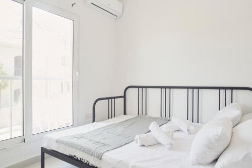 a white bedroom with a bed with pillows and a window at Belleville by Shmoo in San Ġwann