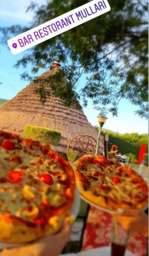 two pizzas on plates on a table with a thatch hut at Bujtinat te Mullari 