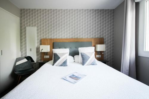 a bedroom with a white bed with a magazine on it at Logis Hôtel l'Amandier in Morlaas