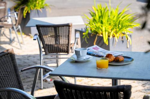 a table with a plate of food and a cup of orange juice at Logis Hôtel l'Amandier in Morlaas