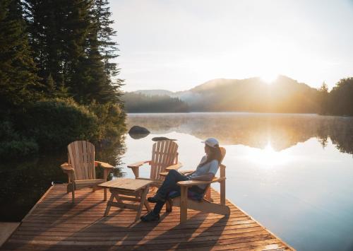 a woman sitting on a bench on a dock near a lake at Huttopia Les Deux Lacs - Laurentides in Mont-Blanc