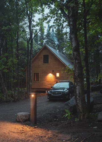 a car parked in front of a cabin in the woods at Huttopia Les Deux Lacs - Laurentides in Mont-Blanc