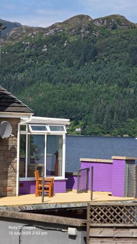 a purple house with a deck next to the water at Jenny's Bay with Hot Tub in Lochgoilhead