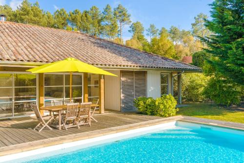 une maison avec une piscine et une table avec un parasol jaune dans l'établissement Lagrange Vacances La Clairière aux Chevreuils, à Moliets-et-Maa
