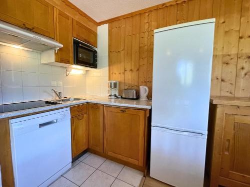 La cuisine est équipée d'un réfrigérateur blanc et de placards en bois. dans l'établissement Appartement 8-10 pers, balcons, proche commerces, pied des pistes - Reberty 1850, Les Ménuires - FR-1-452-92, aux Menuires