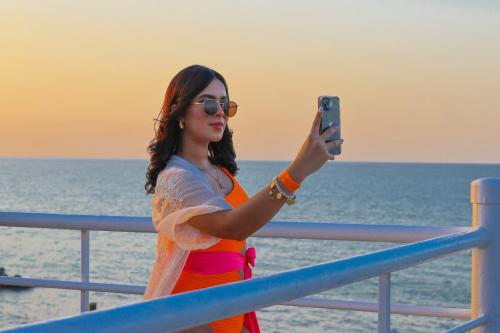 a woman taking a picture of the ocean with her cell phone at Hotel Partenon Beach in La Ceiba
