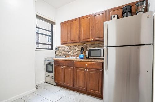 a kitchen with wooden cabinets and a stainless steel refrigerator at Chic 2BD Upper East Side Retreat in New York