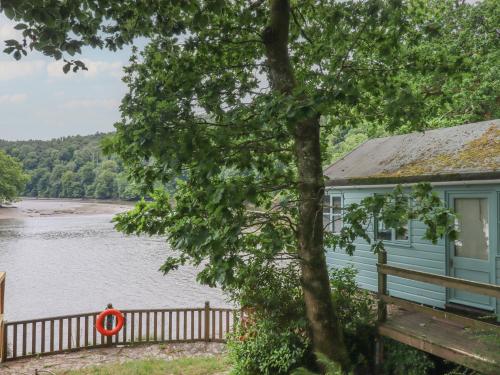 a blue house with a tree and a lake at The Sharpham Boat House in Totnes