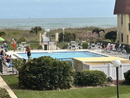 people sitting around a swimming pool with the ocean in the background at Poolfront 2BR Condo with BBQ Steps To Beach & Pier in Cocoa Beach