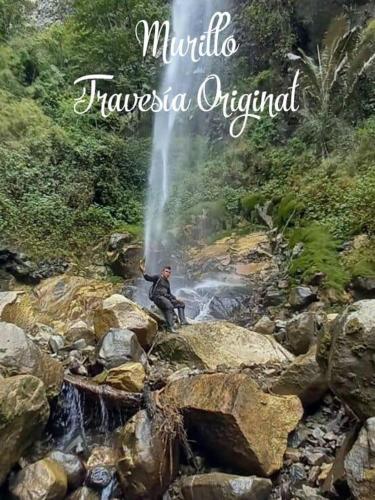 a man sitting on rocks in front of a waterfall at Cabaña Dos Búhos in Murillo