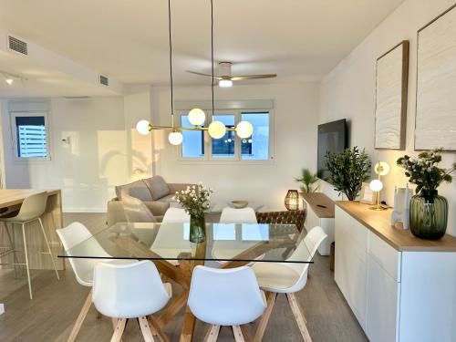 a dining room and living room with a glass table and white chairs at Playa Granada Apartamentos Moriscos II in Motril
