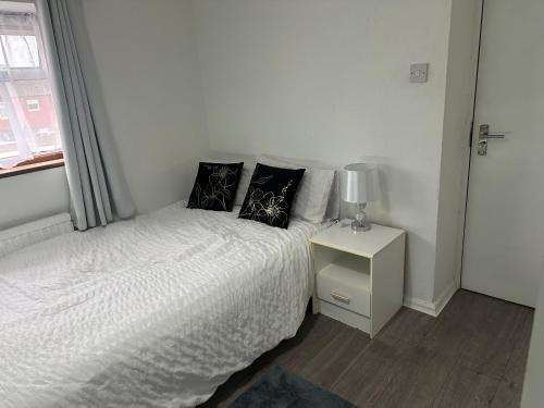 a white bedroom with a bed and a lamp on a night stand at Comfortable Room Near Stacey's Corner Basildon in Basildon