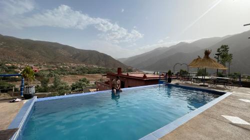 a man standing in a swimming pool with mountains in the background at Ouirgane discovery lodge in Ouirgane