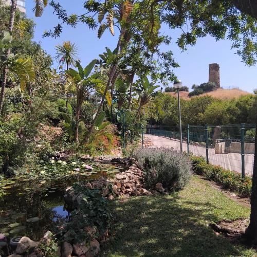 a garden with a pond and trees and a fence at Benalmadena Suite Vistas panorámicas, 2 piscinas, Area infantil, Bar, Jardines y Tenis in Benalmádena
