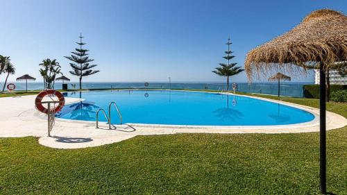 a large swimming pool with a straw umbrella and the ocean at Benalmadena Suite Vistas panorámicas, 2 piscinas, Area infantil, Bar, Jardines y Tenis in Benalmádena