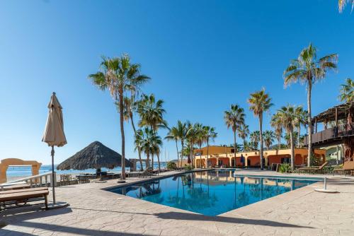 a swimming pool with palm trees and a umbrella at Hotel Playa Del Sol in Los Barriles