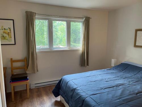 een slaapkamer met een bed, een raam en een stoel bij Le Refuge des Eaux Vives in La Macaza