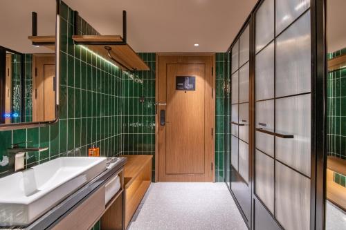 ein Badezimmer mit grün gefliesten Wänden und einer Holztür in der Unterkunft Orange Beijing Yanqing Badaling Great Wall Hotel in Xibozi