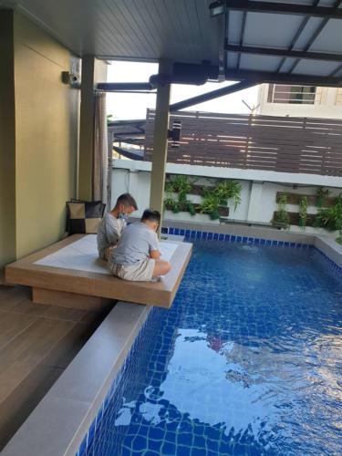 two people sitting on a bench next to a swimming pool at สุวรรณภูมิอพาร์ทเม้นท์ in Suvarnabhumi Airport