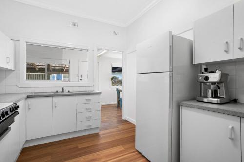 a white kitchen with white appliances and wooden floors at 17 Cypress Street in Evans Head