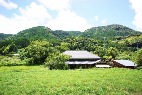 a house in a field with mountains in the background at 農ある暮らしの宿古民家天地 in Minamiizu