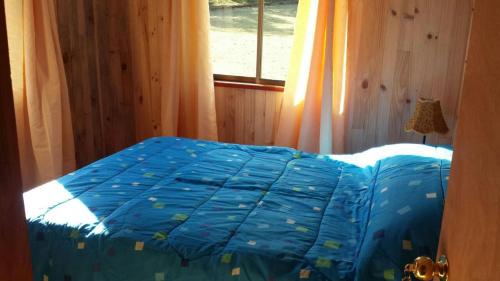 a bedroom with a bed with a blue comforter and a window at Cabañas Los Canelos Hermosa granja en Pucón in Pucón