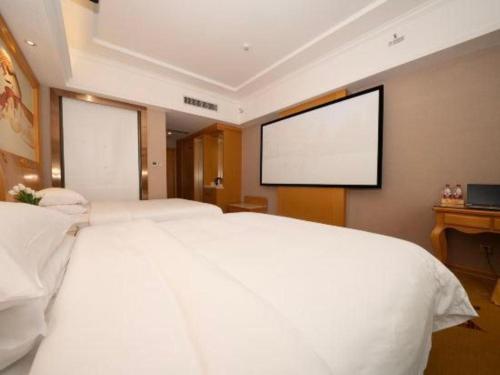 a bedroom with a large white bed and a screen at Vienna Hotel Guangxi Fangcheng in Fangcheng