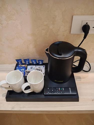 a black tea pot sitting on a counter with three cups at Hotel Coastal Palace in Malpe