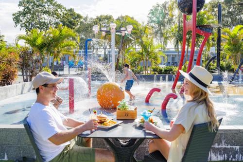 a man and woman sitting at a table in front of a water park at NRMA Treasure Island Holiday Resort in Gold Coast