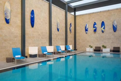 a pool with blue and white chairs next to a wall at Aloft Dhahran Hotel in Al Khobar