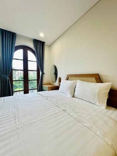 a bedroom with a large white bed with a window at Momento Phu Quoc Hotel in Phu Quoc