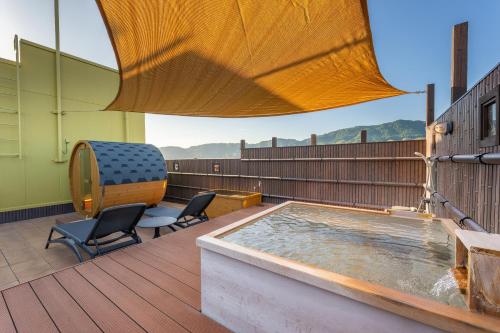a hot tub sitting on a deck with two chairs at Kiyonoya in Asakura
