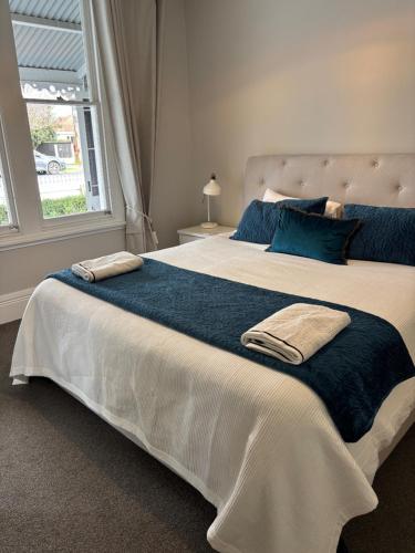 a large white bed with blue pillows and a window at Luxury Village Villa 200metres from Village in Havelock North