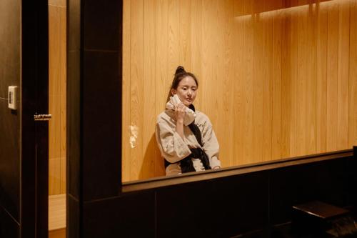a woman wiping her face in front of a mirror at Cave Ryokan Hotel by Aank Sungshin Women's University in Seoul