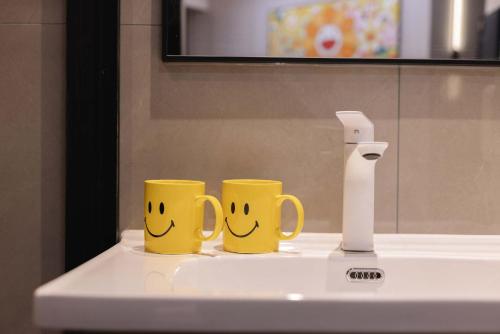 two yellow mugs with smiling faces sitting on a bathroom sink at The Bund River Prologue Residence in Shanghai