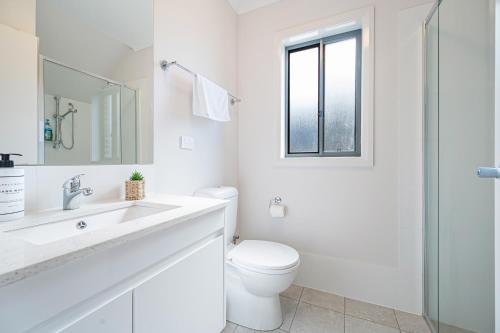 a white bathroom with a toilet and a sink at Warm cozy 5Br house near train station & Coles in Leppington