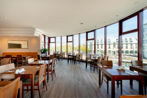 a restaurant with tables and chairs and large windows at Rugs Hotel Augsburg City in Augsburg