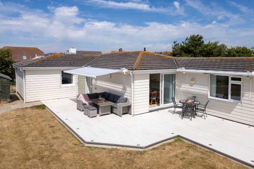 a white house with a deck with a table and chairs at 3-Bed Beach Bungalow & Garden 150m to Sea in West Wittering