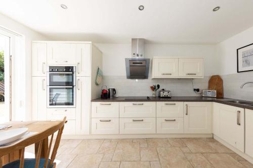 a kitchen with white cabinets and a wooden table at 3-Bed Beach Bungalow & Garden 150m to Sea in West Wittering