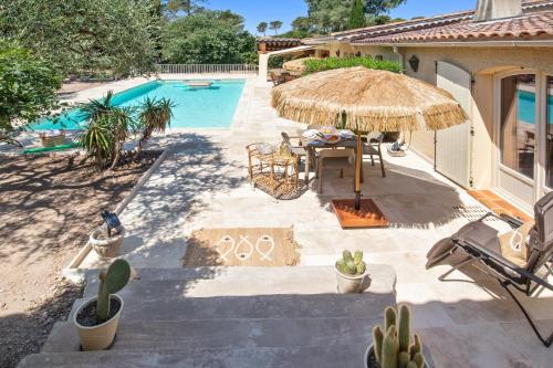 un patio avec une table et un parasol en paille et une piscine dans l'établissement Chez Nous Baraille - Appt climatisé avec piscine, à Puget-sur Argens