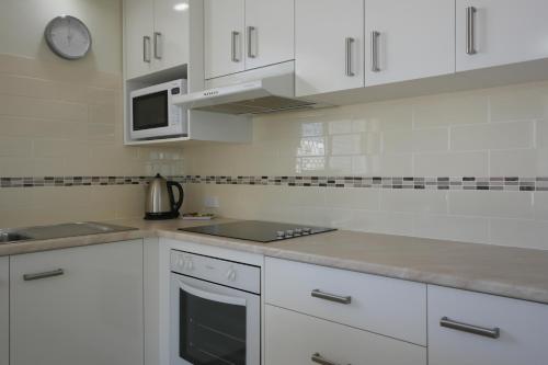 a kitchen with white cabinets and a sink and a microwave at Merrima Court Holidays in Caloundra