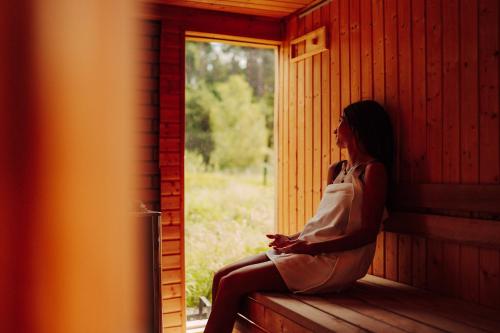 a woman sitting on a window sill in a cabin at Nowoczesne Domki na Drzewie - Kołobrzeg - Sauna - PolanaGlamp in Nieżyn