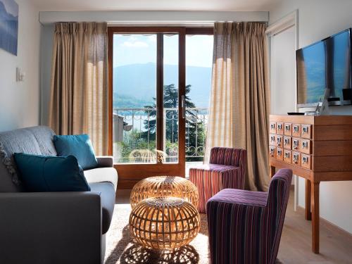 a living room with a couch and chairs and a large window at Hôtel Beau Site Talloires B SPA in Talloires