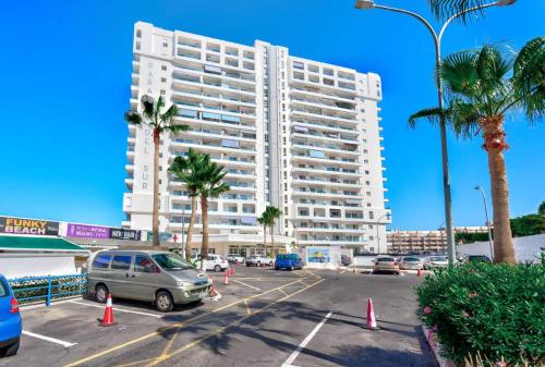 ein großes weißes Gebäude mit auf einem Parkplatz geparkten Autos in der Unterkunft Feels like home in Paraiso in Adeje